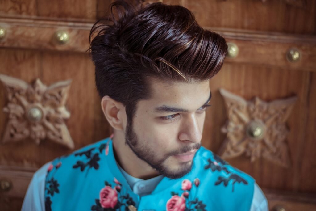 Home Close-up of a fashionable man with styled hair and beard wearing a floral vest indoors.