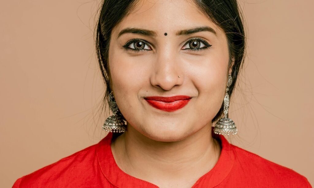 Home Charming close-up portrait of a South Asian woman with red lipstick and traditional jewelry.